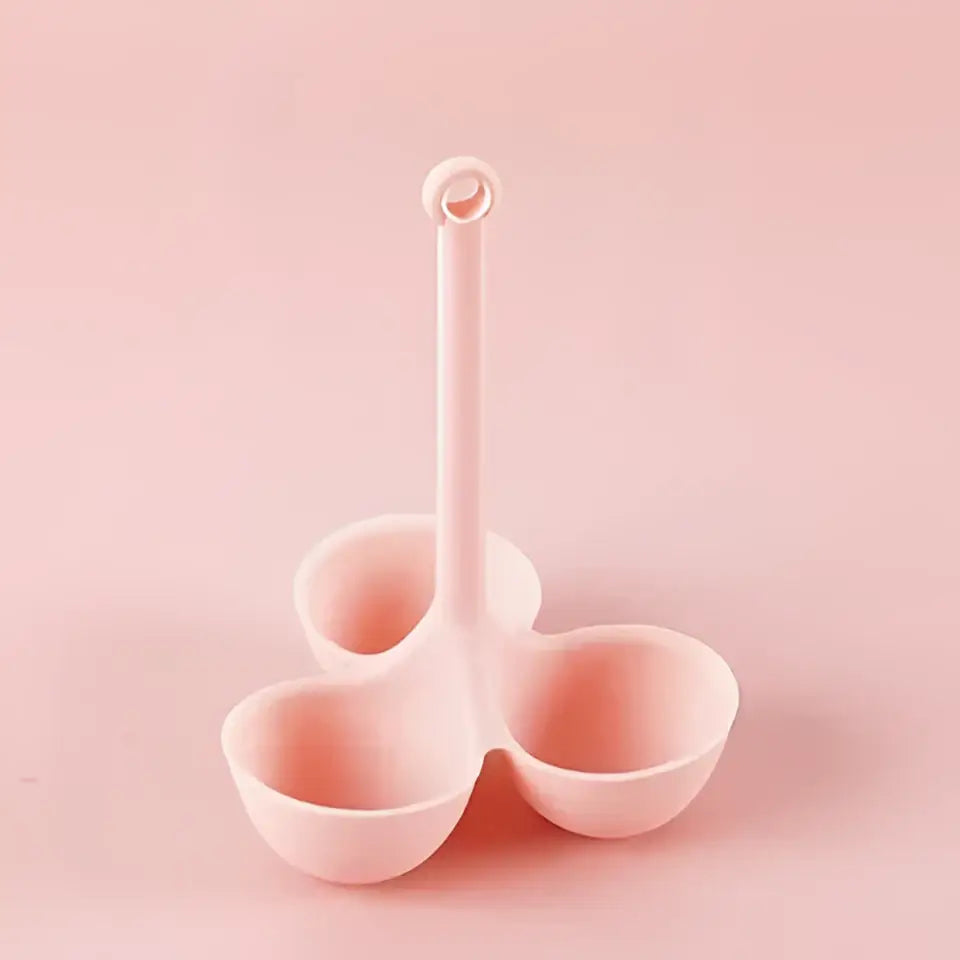 Pastel pink plastic three-compartment serving spoon with looped handle for pink and lavender silicone egg steamer tray holder