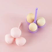 Pink and lavender silicone egg steamer tray with three rounded compartments holding pale yellow eggs for kitchen use