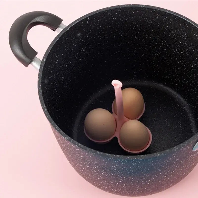 Pink silicone egg steamer tray with three compartments holding brown eggs inside a black speckled pot for kitchen use