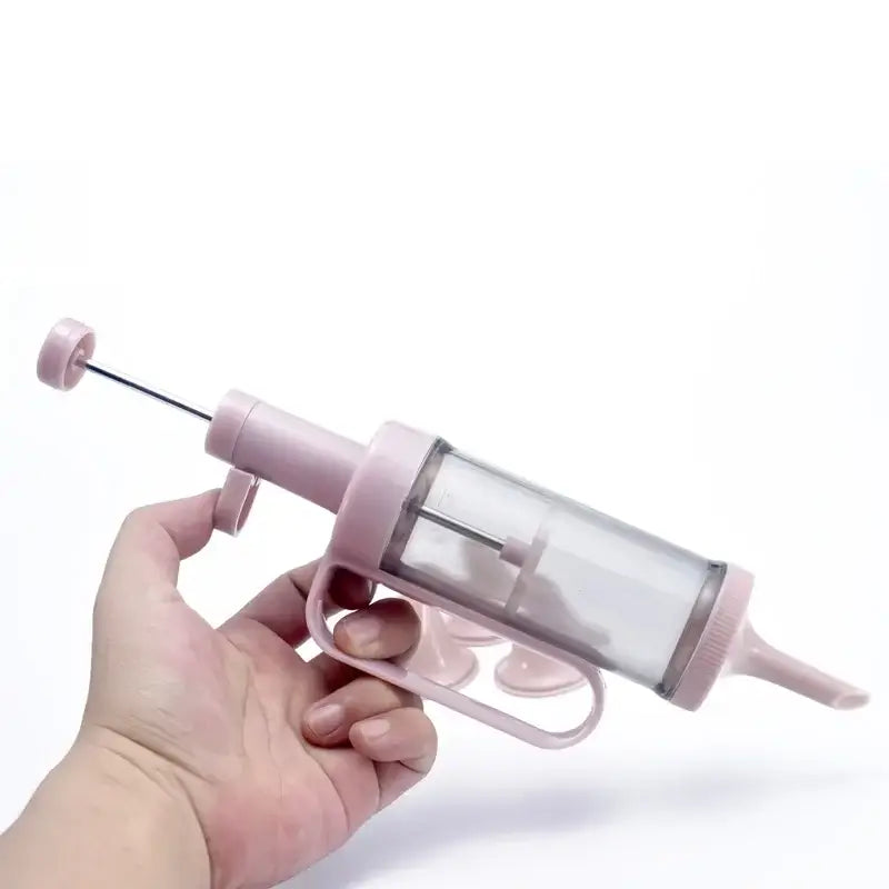 Pink plastic cream decorating gun with clear cylindrical chamber and metal plunger rod for kitchen baking set