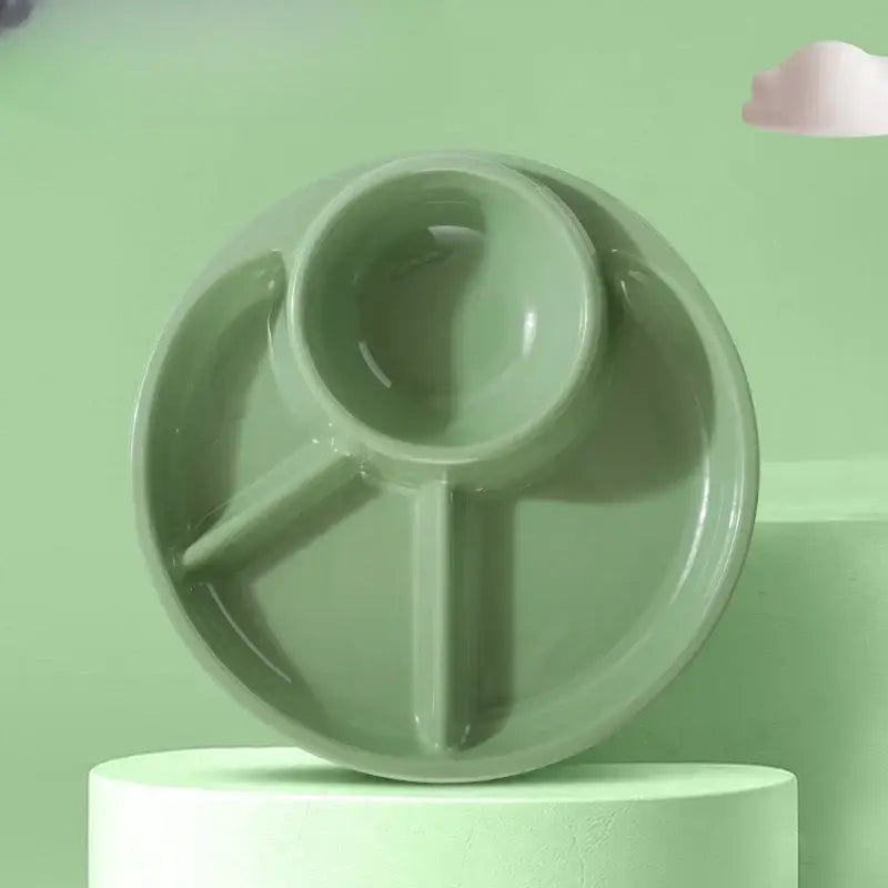 A matte sage green ceramic portion control plate with three compartments including a spoon-shaped section for kids meals