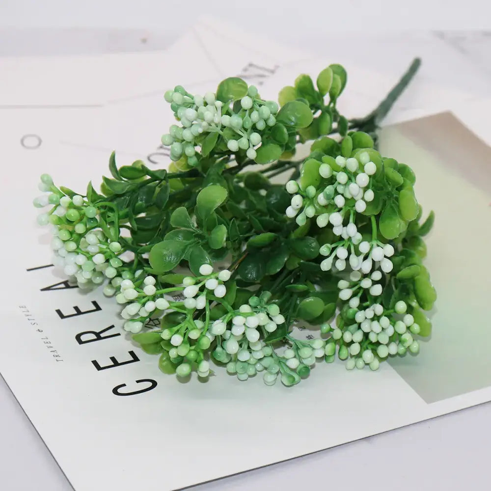 A cluster of artificial green foliage with white berries made of plastic for pink and purple succulent branch plant wall decor
