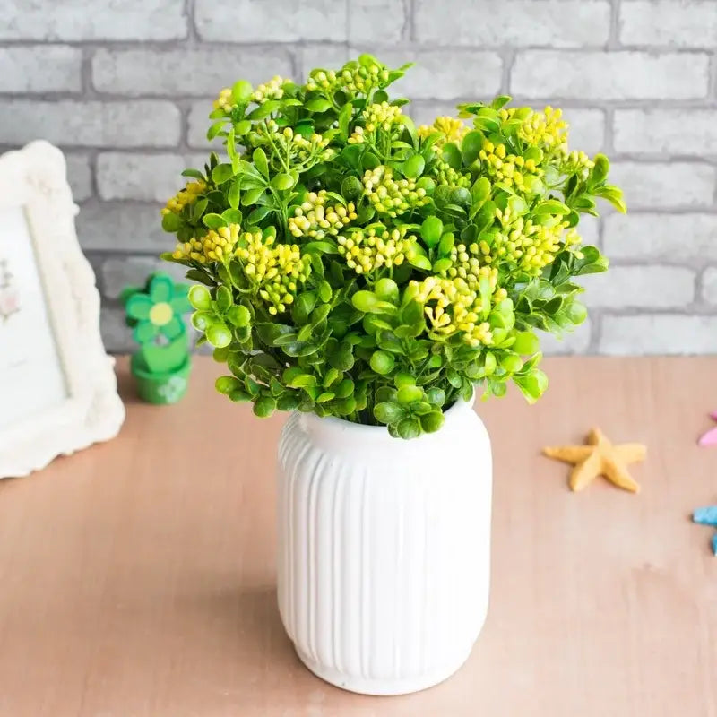 A lush green and yellow artificial branch plant wall arrangement in a white ribbed ceramic vase for plant wall decor