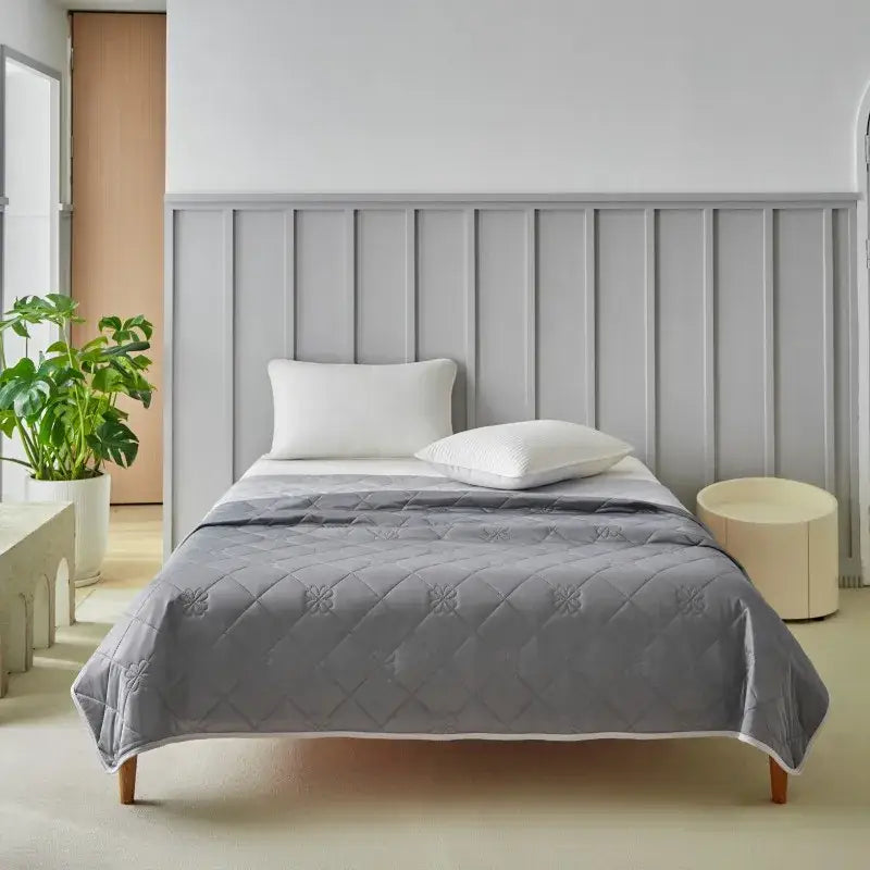 Gray quilted summer blanket with subtle floral pattern and white piping providing cool summer comfort