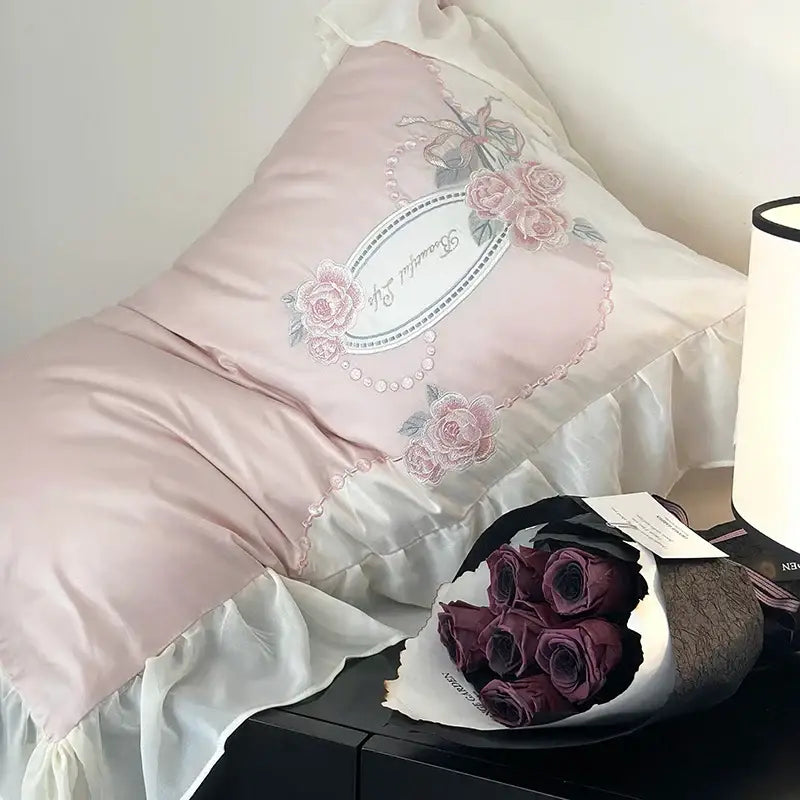 A soft pink satin pillow with delicate floral embroidery and pearl trim from an egyptian cotton flowers bedding set