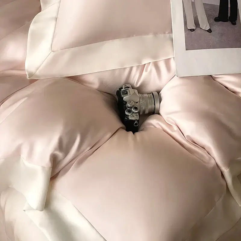 A sleek silver and black vintage camera rests on a blush pink satin eucalyptus fiber bedding set by decorbites