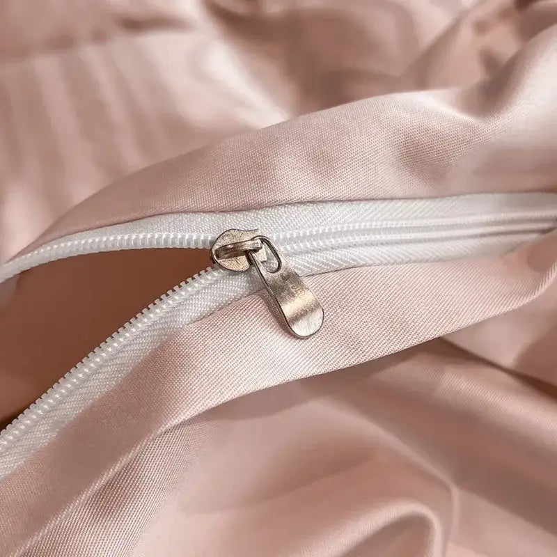 A sleek metallic zipper on soft pink satin jacquard fabric with white piping in a duvet cover set