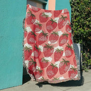 A pink knitted blanket with red cat strawberry patterns and white clouds, edged with fringed tassels for bedroom decorbites