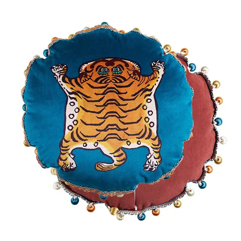 A plush blue velvet circular cushion cover with an embroidered orange tiger cat print and decorative tassels