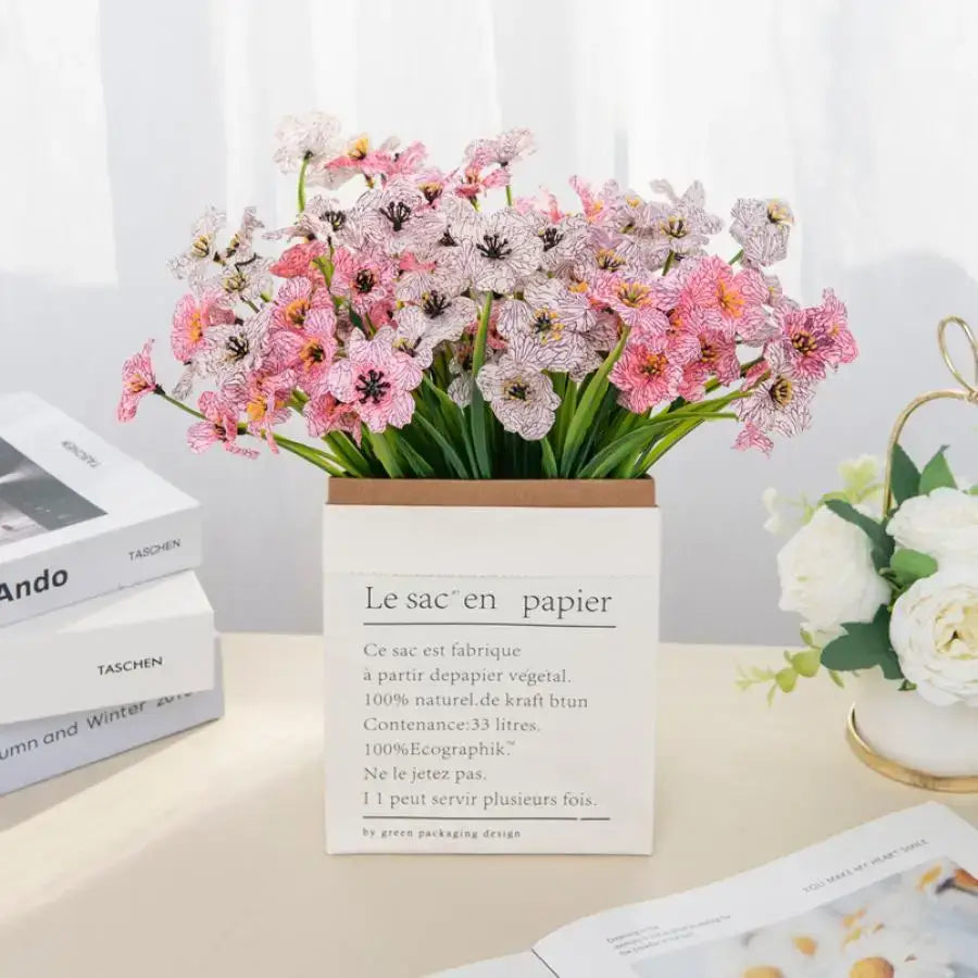 A delicate arrangement of pink and white artificial cherry blossoms with black centers in a square paper box for wedding decor