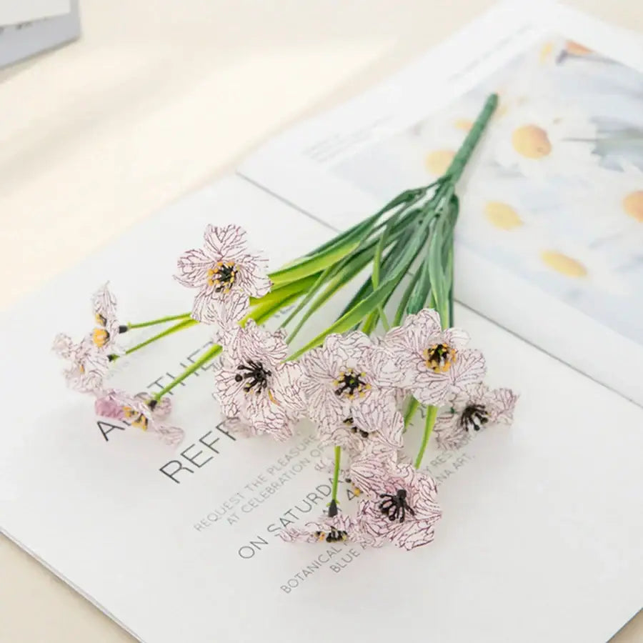 A delicate cluster of pale pink and white artificial cherry blossoms with dark centers on slender green stems for wedding decor
