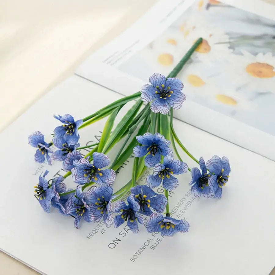 A delicate cluster of artificial blue cherry blossoms with white veining on green stems in a wedding decor box