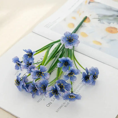 A delicate cluster of artificial blue cherry blossoms with white veining on green stems in a wedding decor box