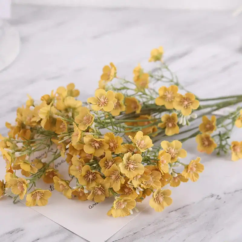 A cluster of artificial yellow flowers with delicate petals and green stems in a decorbites imitation flower bouquet