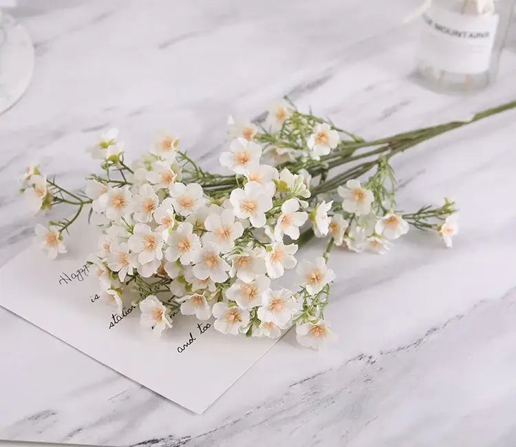Delicate pink and white artificial flowers baby’s breath wedding bouquet with peach centers on marble surface decorbites imitation flower