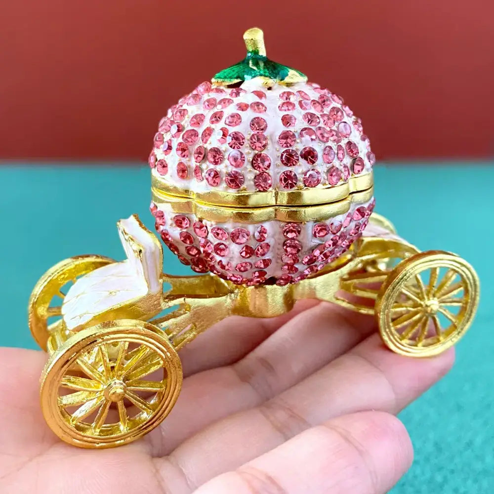 Pink and white rhinestone jewelry trinket box shaped like a crown carriage with gold wheels and green leafy top decor