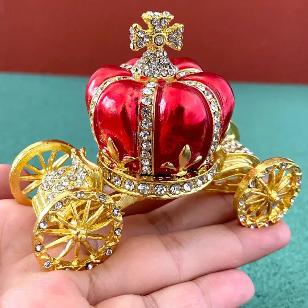 A shiny red and gold jeweled carriage ornament with crystal embellishments on a pink and white rhinestone jewelry trinket box