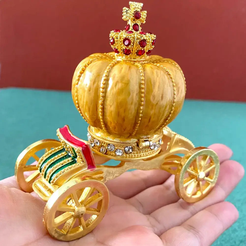 Golden crown-shaped carriage ornament with red gemstones and crystals on pink and white rhinestone jewelry trinket box