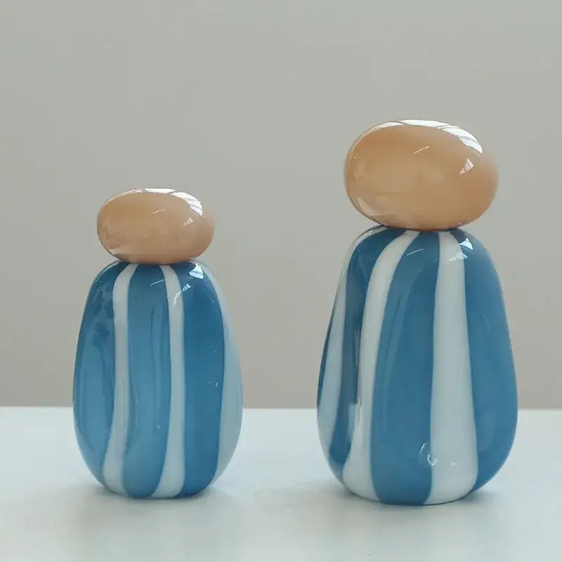 Two glossy blue and white striped glass figurines with beige tops displayed alongside pink and white striped ceramic vase cover band for living room decor
