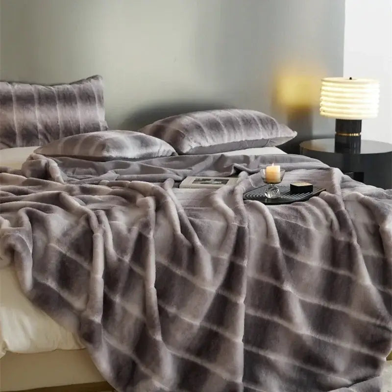 Soft gray faux fur throw blanket with subtle stripes draped over bed from decorbites cozy fleece collection