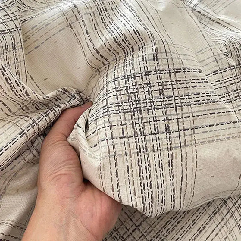 A hand gently holds an off-white plaid cream and charcoal decorbites cotton grid bedding set fabric