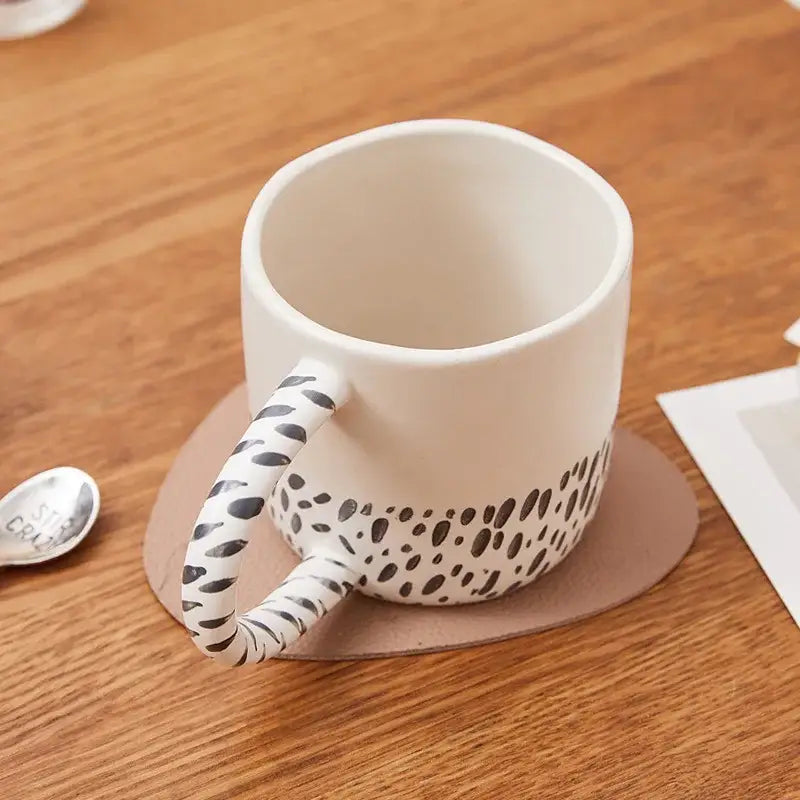 White ceramic coffee milk mug with black spotted pattern and handle resting on brown coaster 340ml ceramic coffee