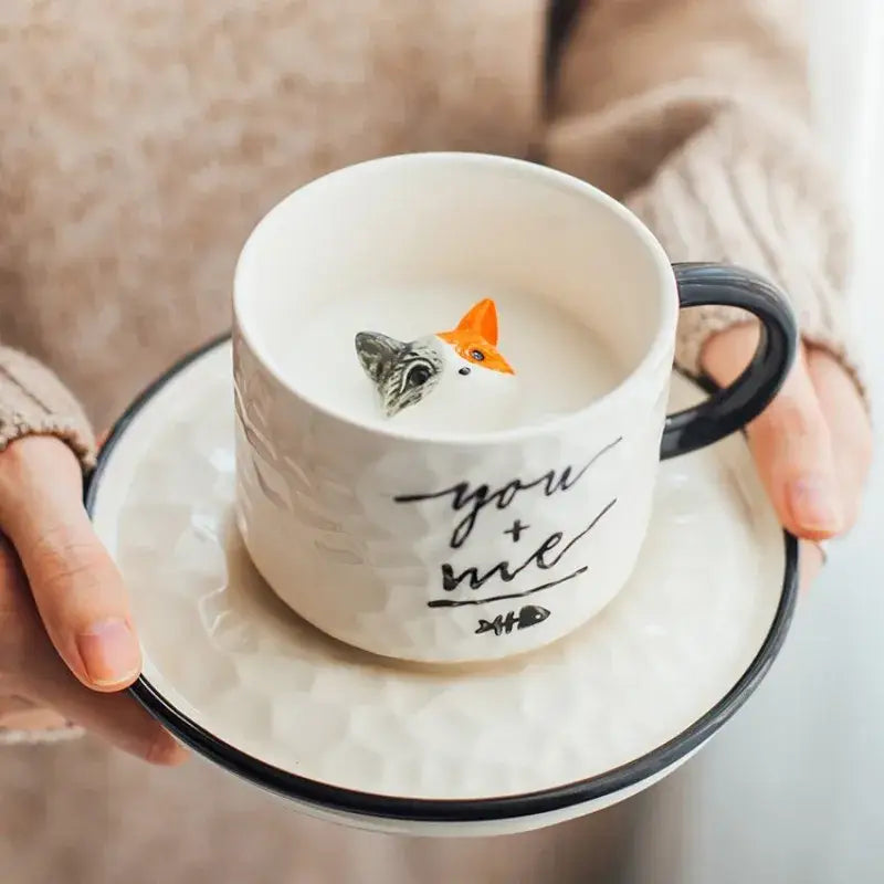 White ceramic cup with black handle and rim featuring a you plus me inscription and orange gray fox figurine inside decorbites cat claw ceramic