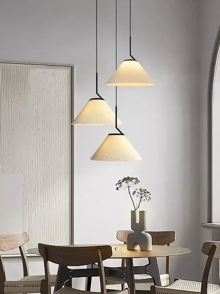 Three cream pleated chandelier pendant lights with black metal fixtures hanging above a dining table decorbites cream led