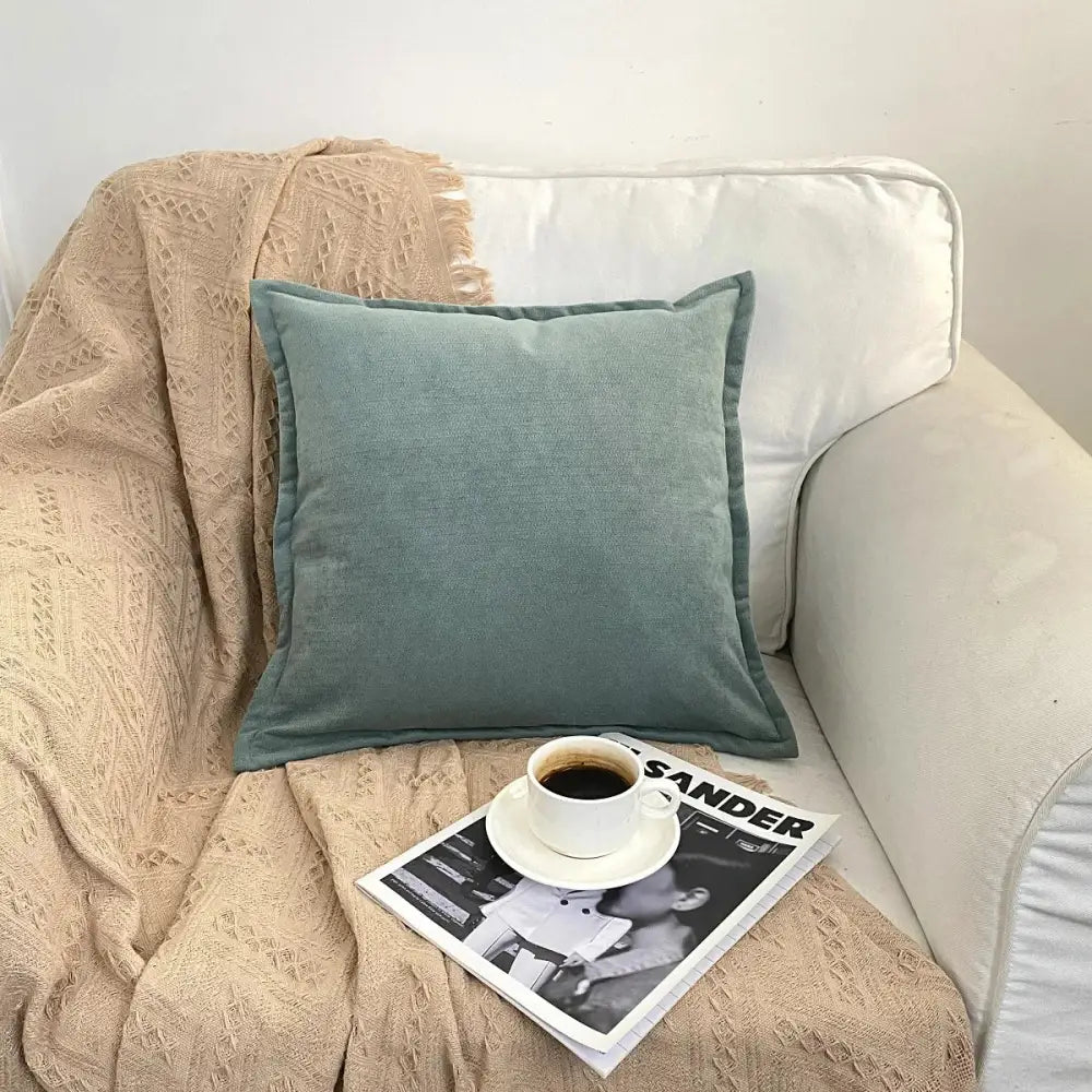 A soft teal square cushion with textured fabric on a beige blanket complements decorbites houndstooth cushion cover decor
