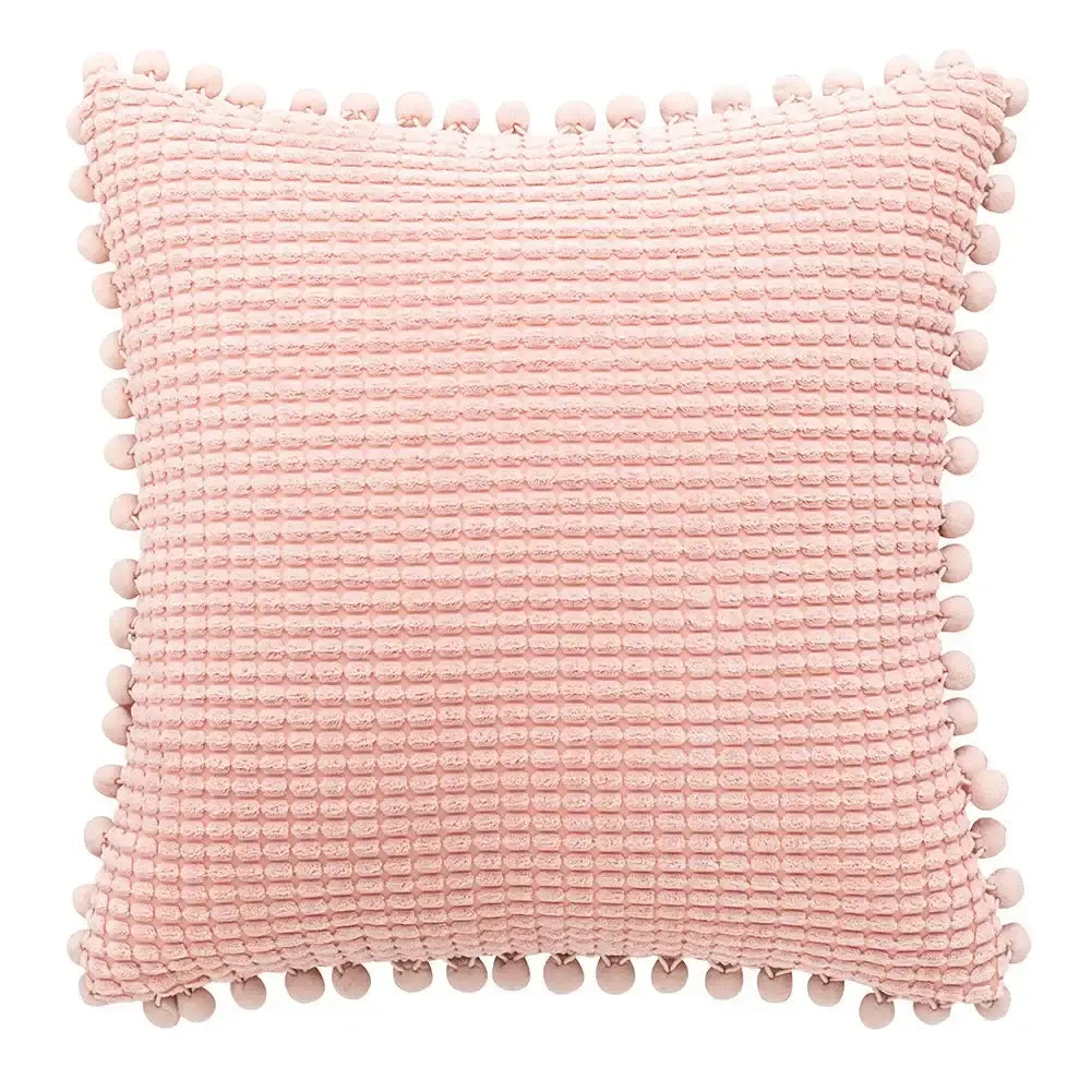 A soft pink waffle-textured pillow with pom-pom trim shown alongside a plush black and white decorbites houndstooth cushion cover
