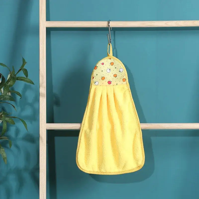 A cheerful yellow coral velvet hand towel with playful fruit pattern hanging from a metal hook by Decorbites