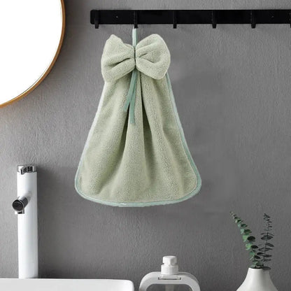 A soft mint green coral velvet hand towel with plush texture and matching bow hangs on a black hook for kitchen or bathroom decorbites coral velvet soft
