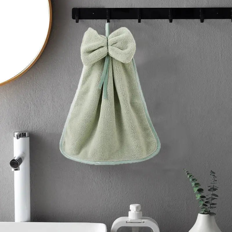 A soft mint green coral velvet hand towel with plush texture and matching bow hangs on a black hook for kitchen or bathroom decorbites coral velvet soft