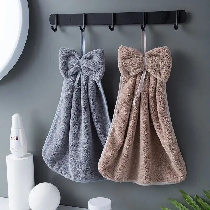 Two plush coral velvet soft hand towels with large bows in gray and beige hang on a black rack for kitchen decorbites