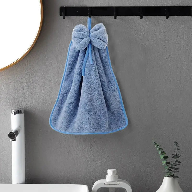 A light blue decorbites coral velvet soft hand towel with plush bow hangs on a black hook for kitchen or bathroom use