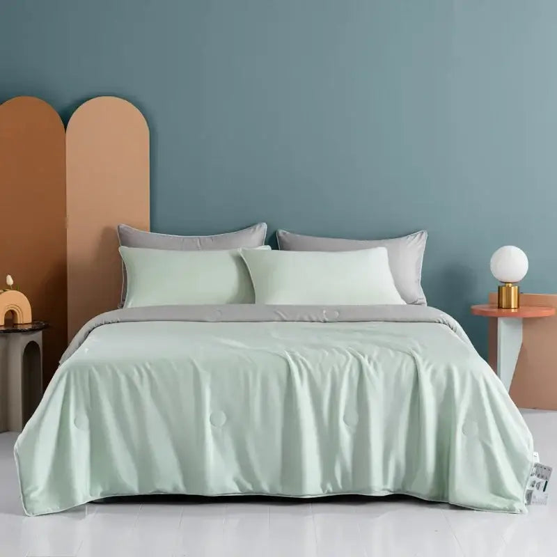 A soft mint green satin decorbites cooling comforter with subtle sheen and matching pillows in a minimalist bedroom