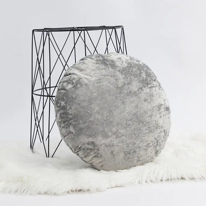 A plush round gray velvet pillow cover with a dark grain texture on a white faux fur rug for living room decor