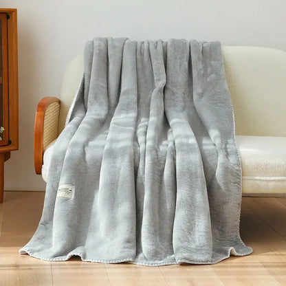 A soft light gray plush double-layer warm blanket with cozy texture and neatly stitched edges for bedroom use
