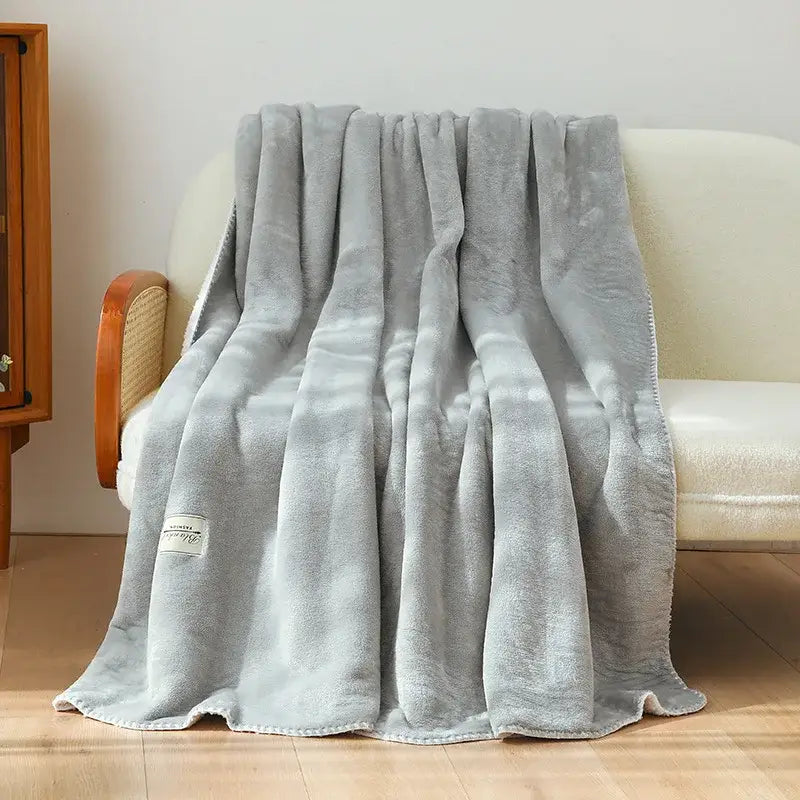 A soft light gray plush double-layer warm blanket with cozy texture and neatly stitched edges for bedroom use