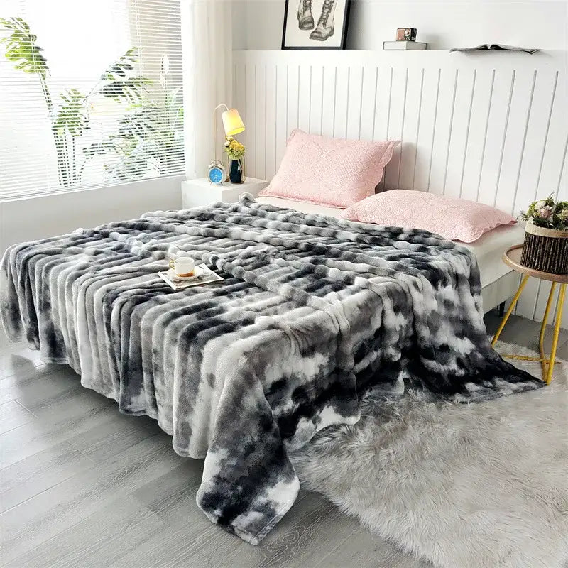 Plush gray and black tie-dye fleece throw blanket made of faux fur draped over bed for living room decor