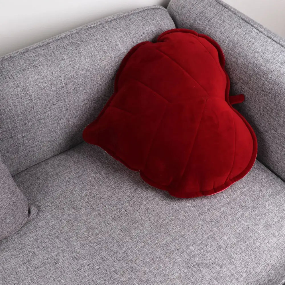 A plush deep red heart-shaped cushion with quilted texture on gray sofa complements decorbites 3d leaf throw pillows