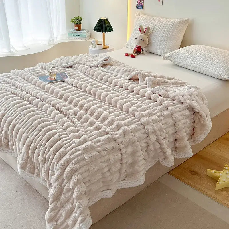 Cream-colored plush chunky knit throw blanket with soft texture paired with plush pink bamboo velvet blanket with braided trim