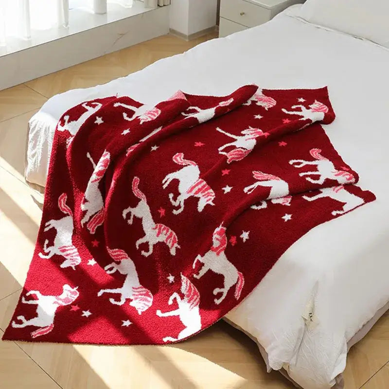 Plush red unicorn blanket made of half fleece red material with white unicorns and stars in a playful pattern