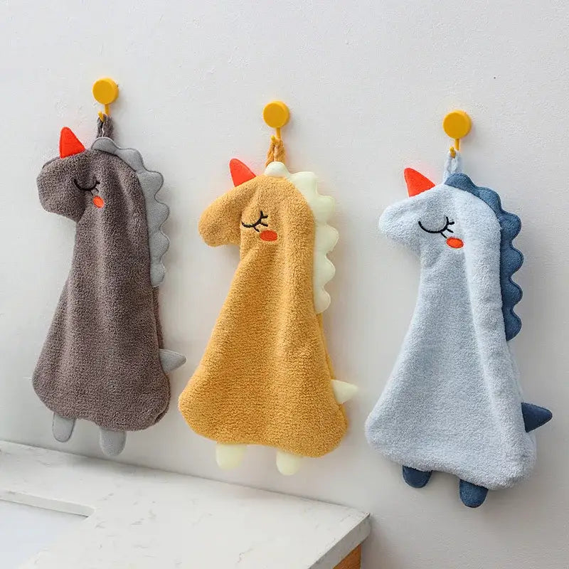 Three plush unicorn hand towels in gray yellow and light blue with orange horns made of double-layer coral velvet hanging from hooks