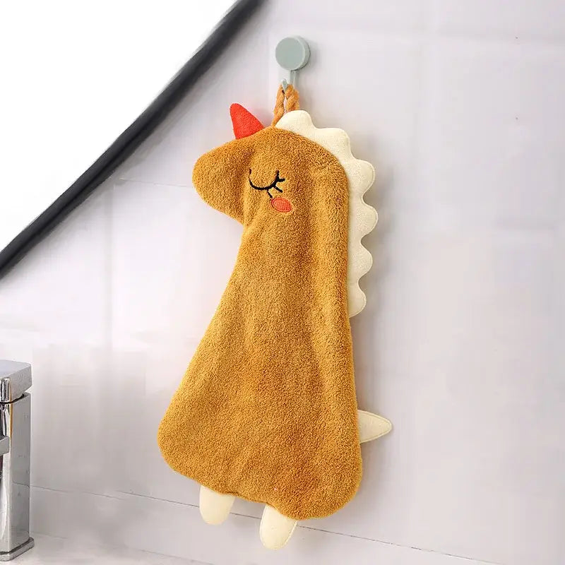 A plush tan unicorn hand towel with red horn and white mane made of double-layer coral velvet hanging from a hook