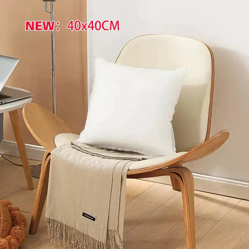 Cream-colored throw blanket with fringe draped over wooden chair beside a plush white decorbites cotton-padded pillow core