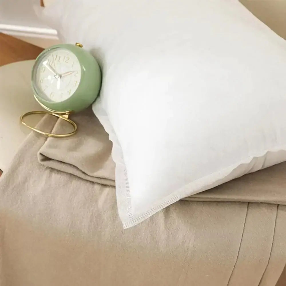 A plush white cotton-padded pillow core with subtle textured edges beside a mint green vintage alarm clock