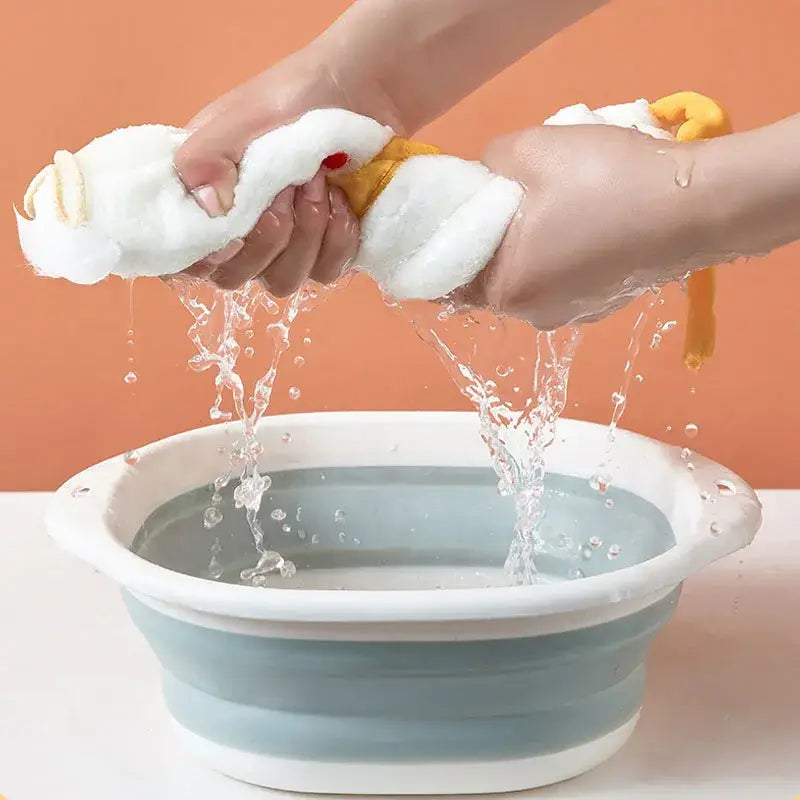 A collapsible silicone basin with a white rim and light blue body shown alongside a plush white and gray duck terry towel kitchen cleaning cloth