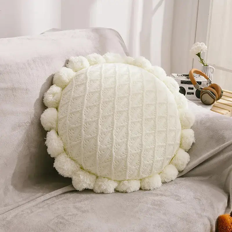 Cream-colored round pillow with textured knit center and pom-pom trim for plush white and soft pink flowers pillows home decor