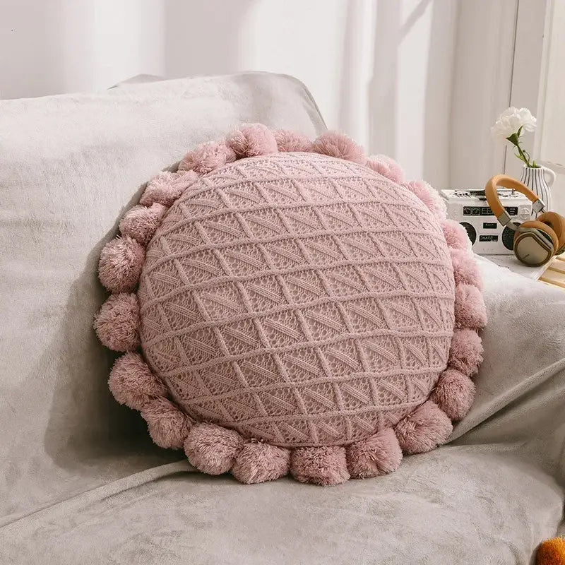 A soft pink knitted round pillow with textured diamond pattern and pom-pom trim for home decor and decorbites 3d flowers pillows